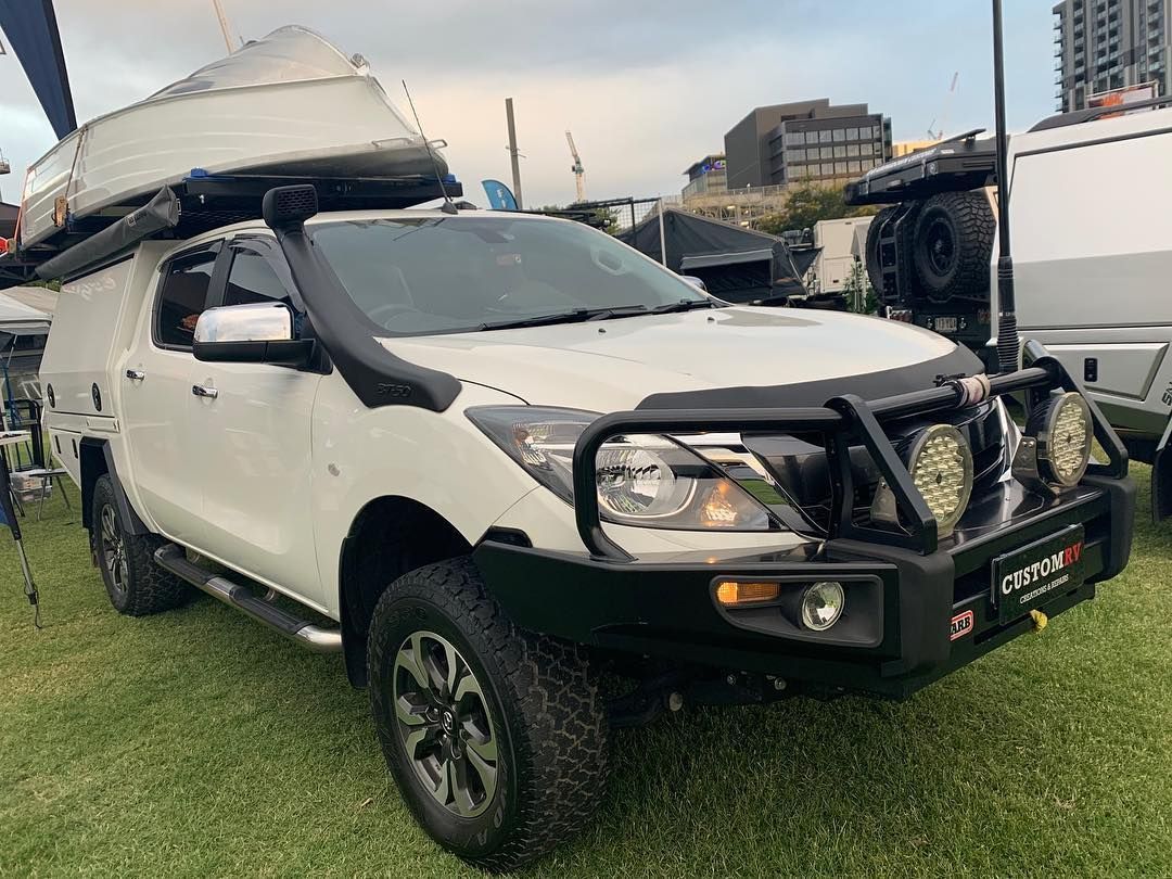 A White Vehicle With a Boat on Top of It is Parked in a Grassy Field — Custom RV Creations in Gold Coast, QLD