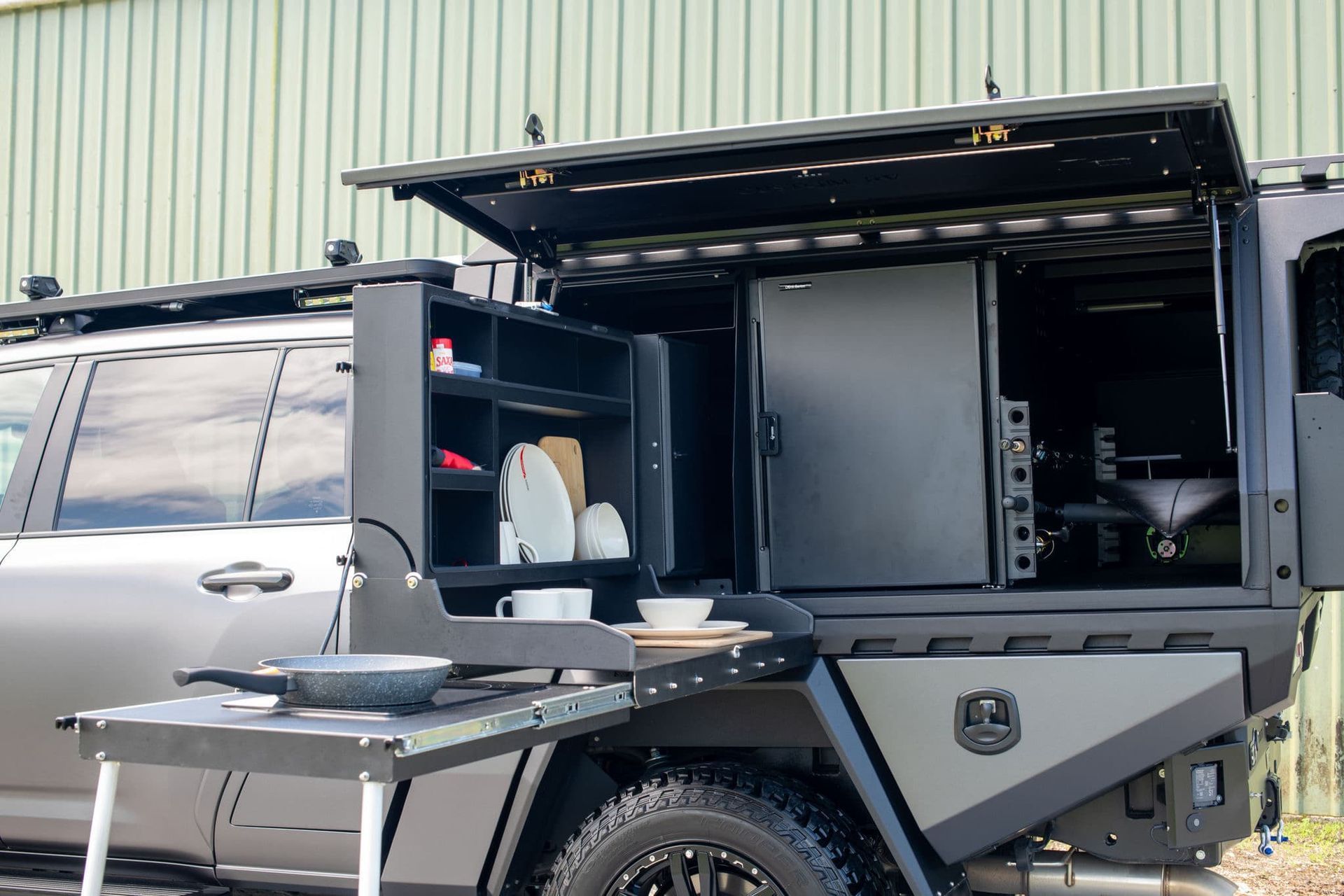 Black Canopy With Open Shelves, Fridge, and Pull-out Cooking Table, Parked by a Green Building — Custom RV Creations in Sumner, QLD