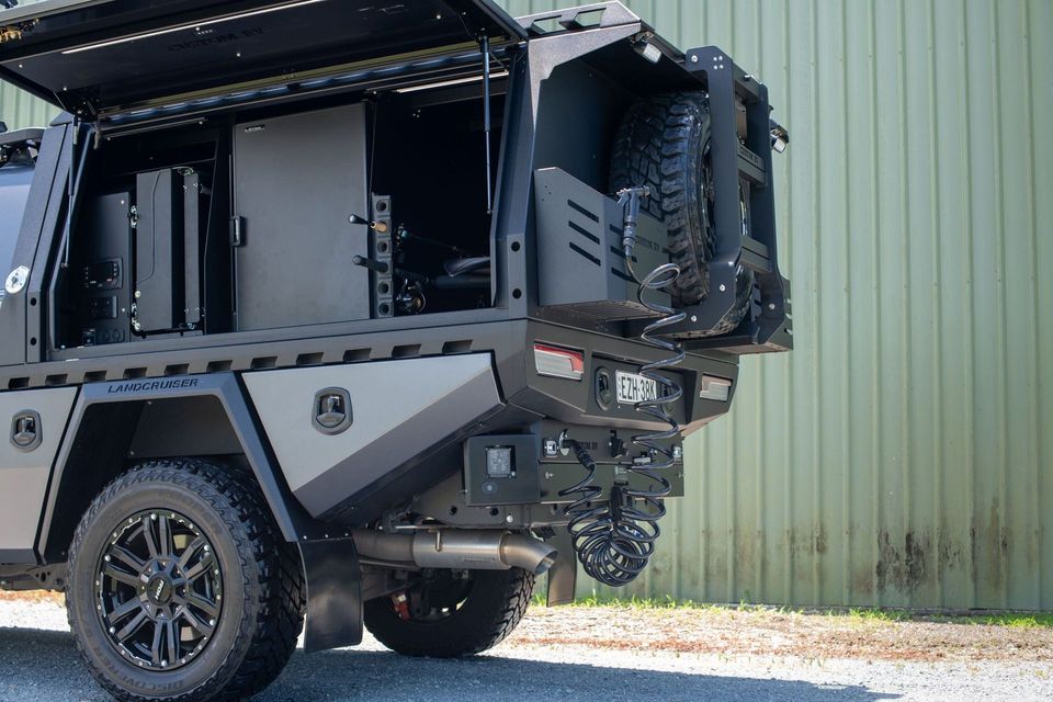Dark Grey Customized Utility Truck With Spare Tire and Equipment, Parked Next to a Green Wall — Custom RV Creations in Sumner, QLD
