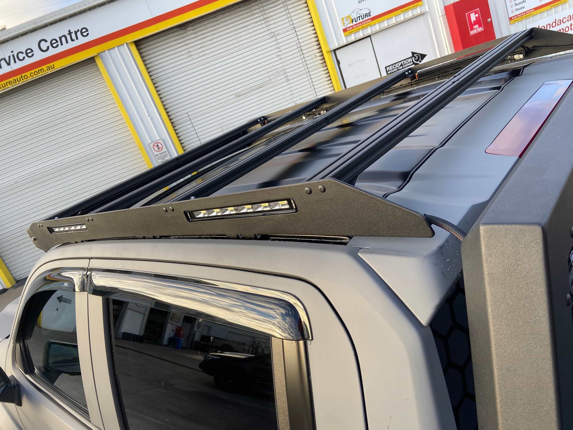 Black Roof Rack With LED Light Bar Installed on a Grey Pickup Truck, Outside a Service Center — Custom RV Creations in Sumner, QLD