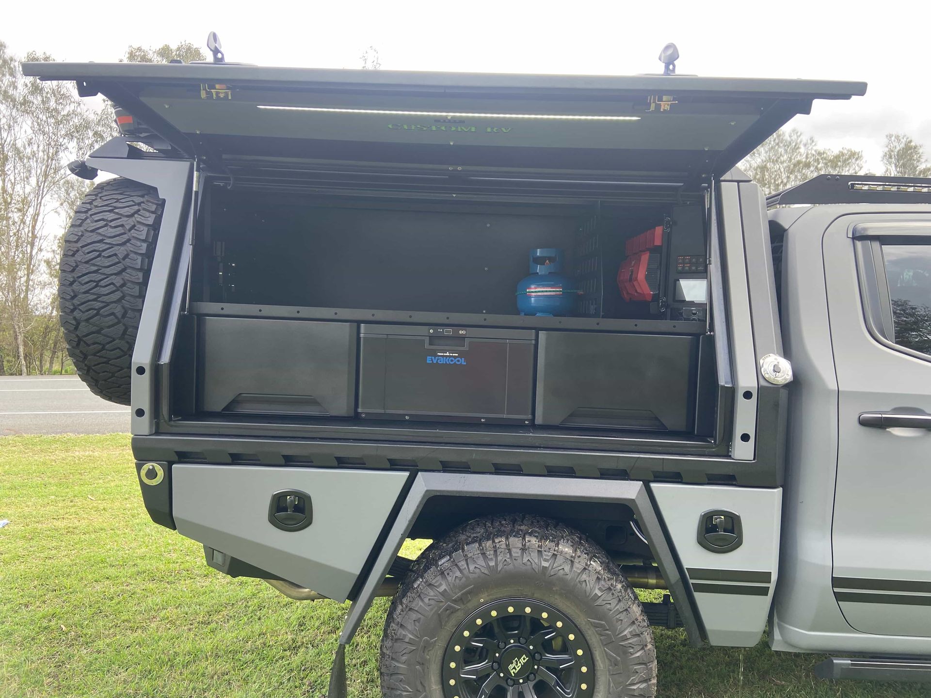 Grey Truck Bed With a Storage Unit, Spare Tire, and Gear. Open Door Reveals Drawers and a Gas Cylinder — Custom RV Creations in Sumner, QLD