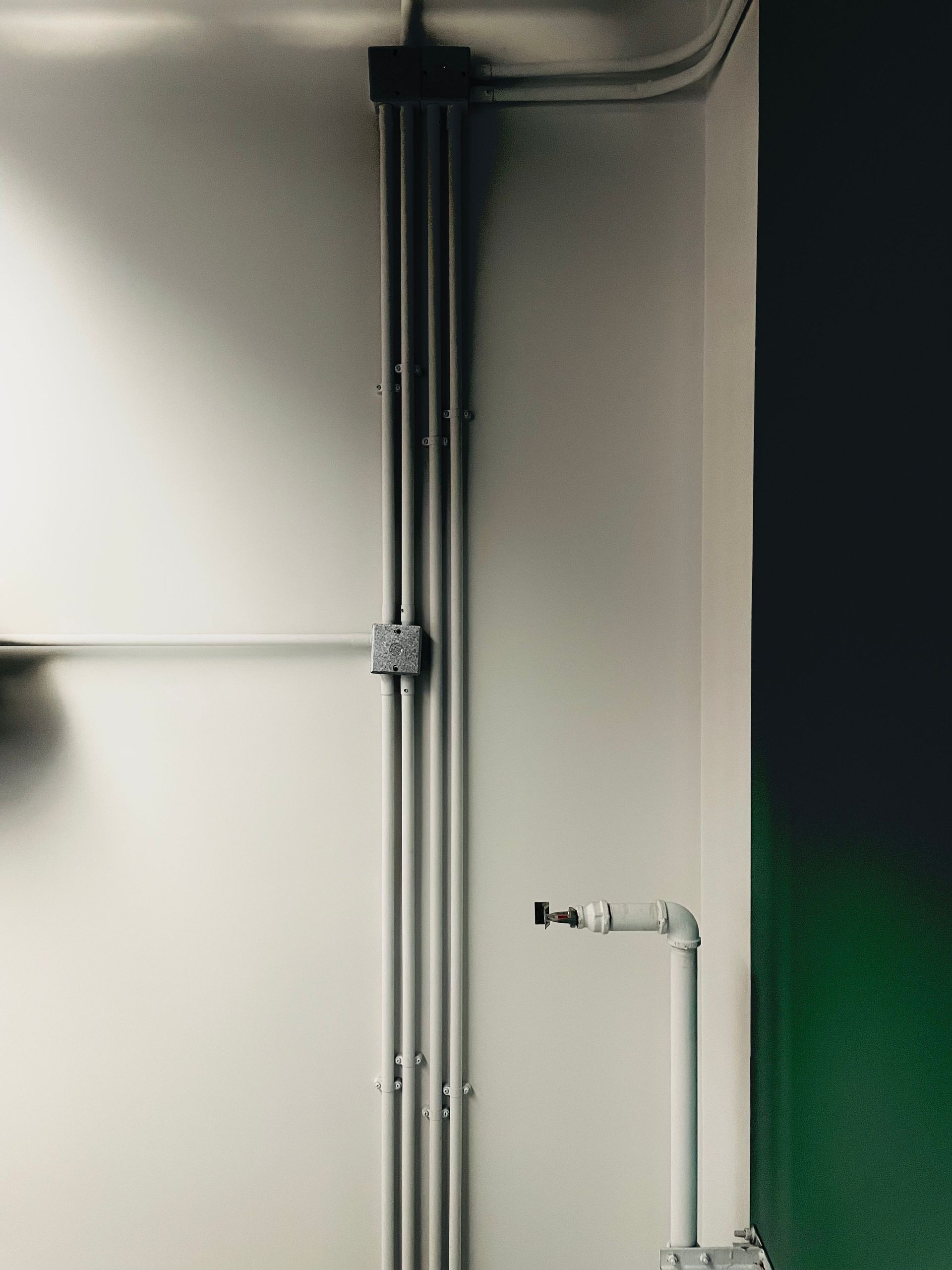 Gray utility pipes mounted on a wall in an indoor corner, with a white pipe valve on the right.