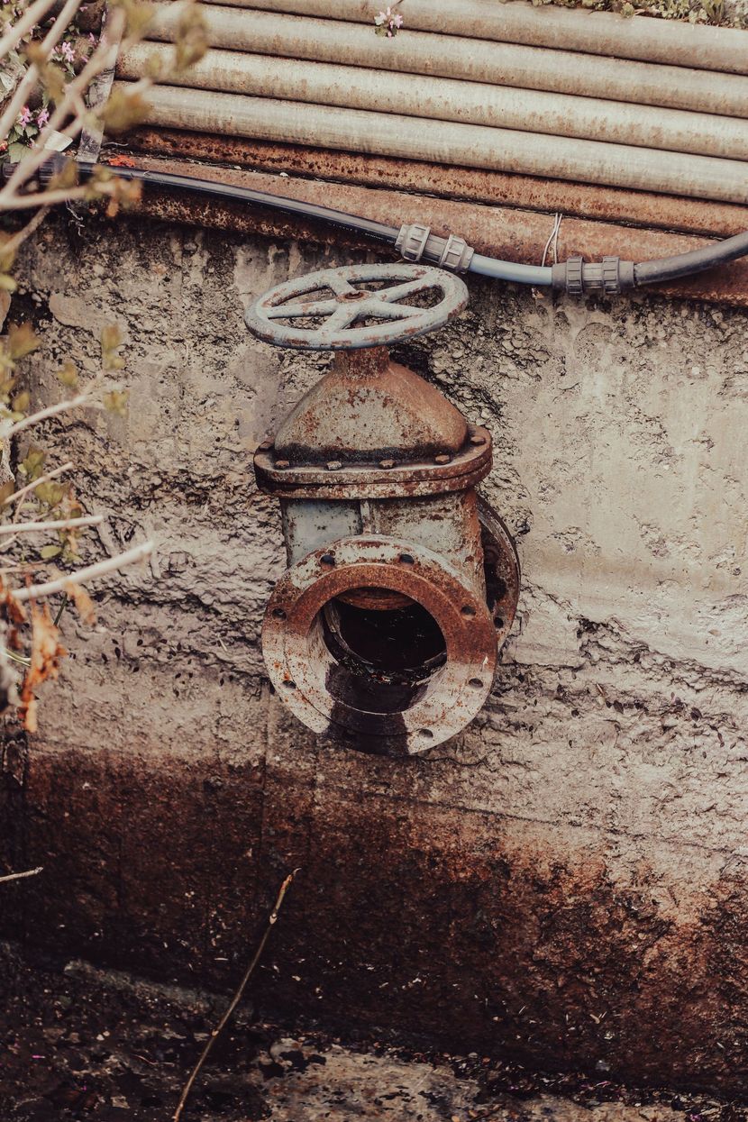Rusty pipe and valve protruding from a weathered concrete wall with dark water below.