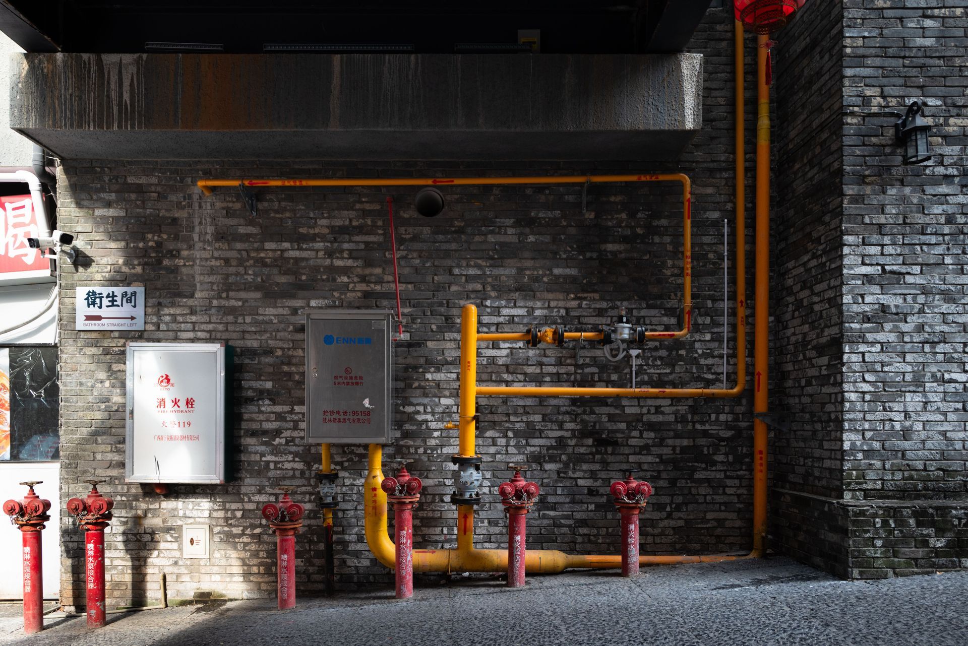 Industrial pipes and valves on a brick wall beside red hydrants under an overhang