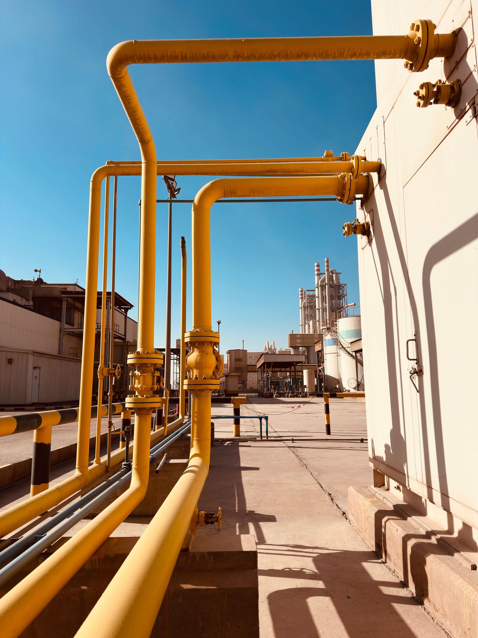 Yellow industrial pipes along a rooftop walkway under a clear blue sky.