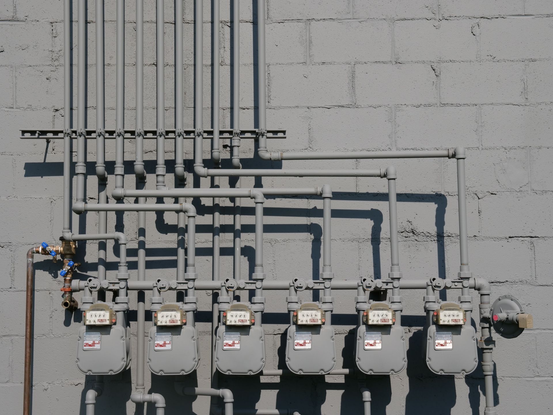 Row of utility meters and conduits mounted on a gray cinderblock wall