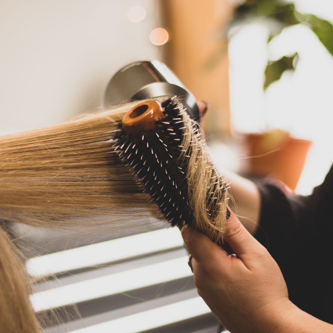 A woman is brushing her hair with a round brush