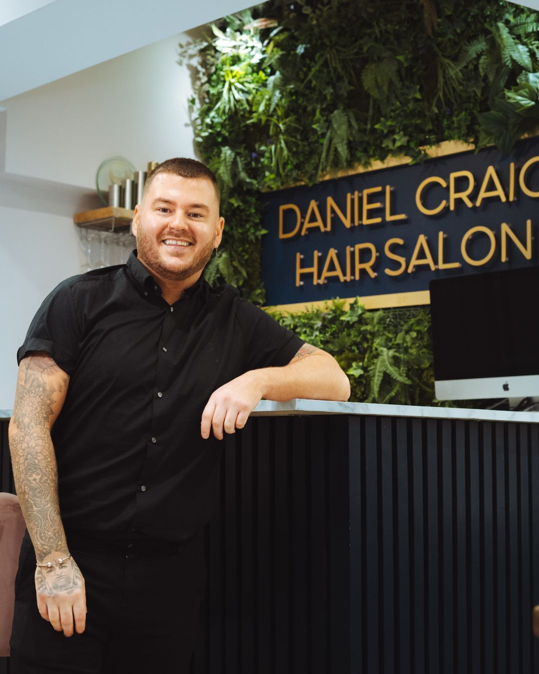 A man is leaning on a counter in front of a sign that says daniel craig hair salon