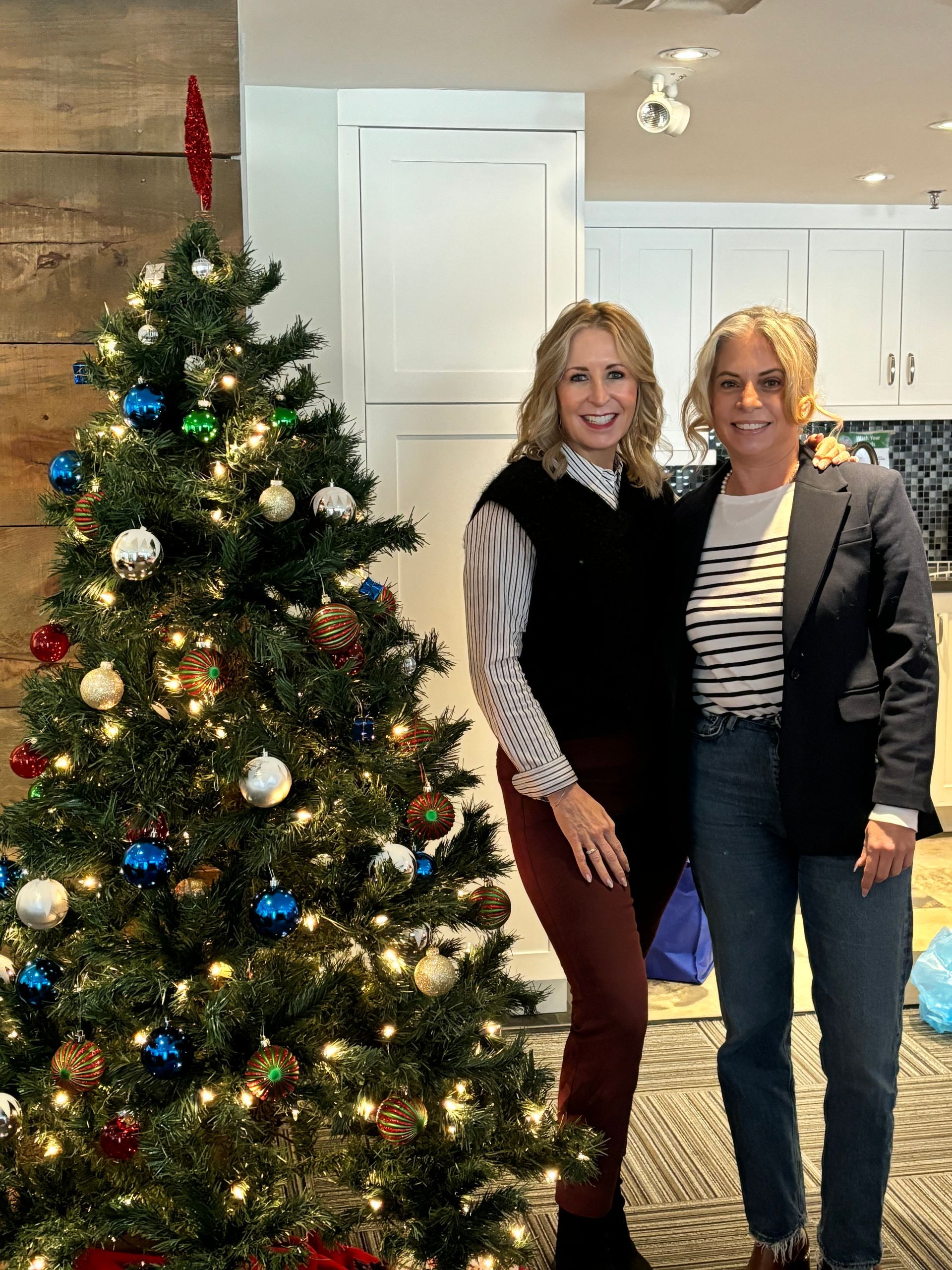 Two women are posing for a picture in front of a christmas tree.