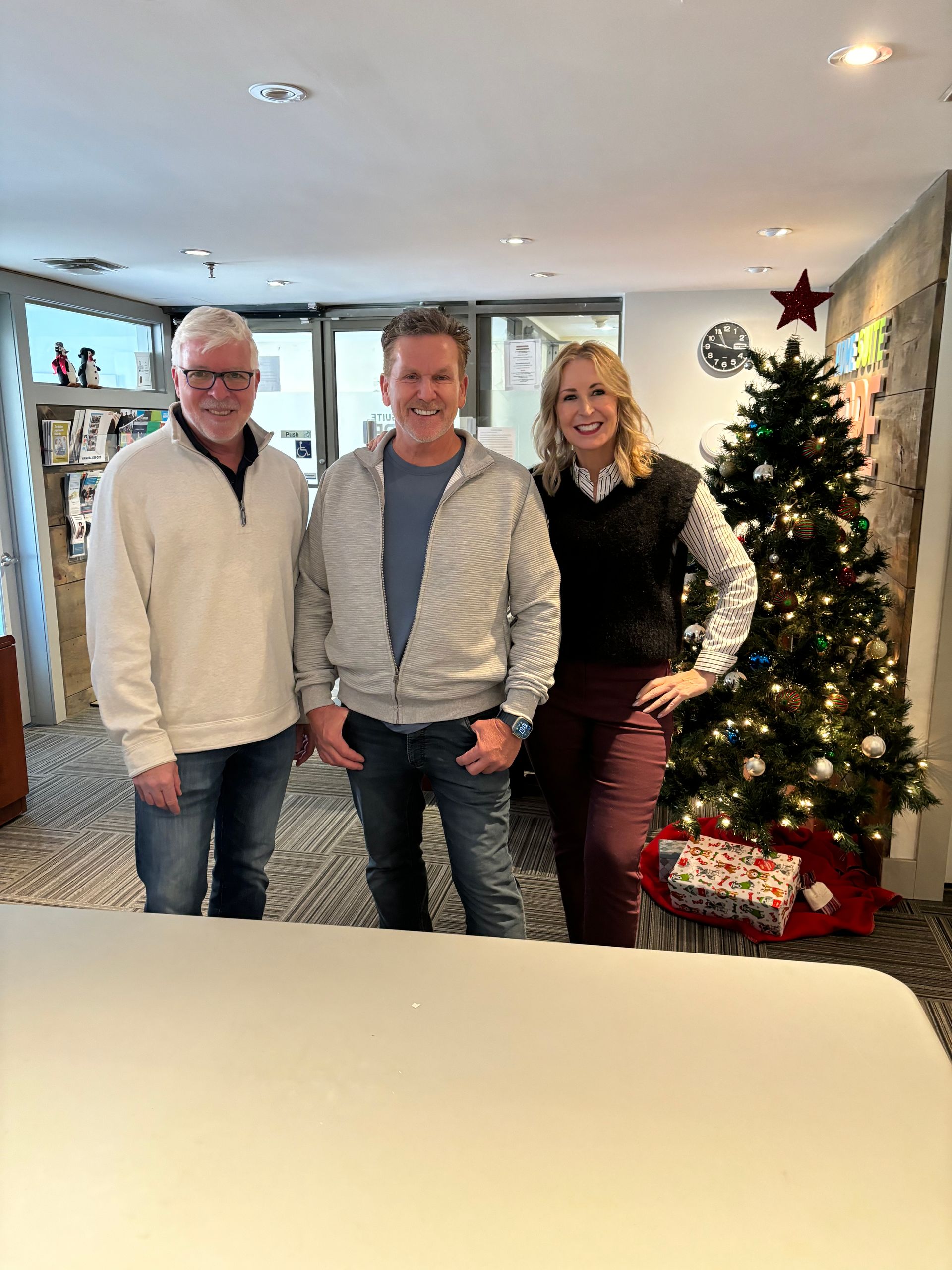 Three people are posing for a picture in front of a christmas tree.