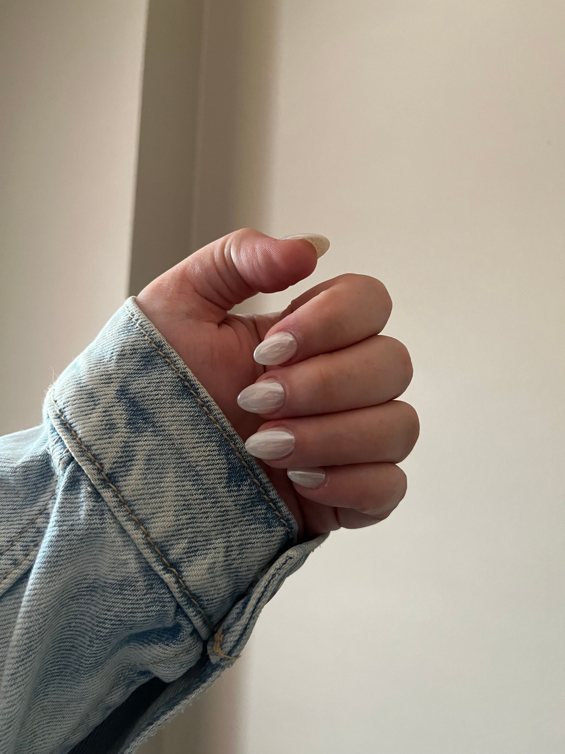 A close up of a person 's hand with white nails and a denim jacket.