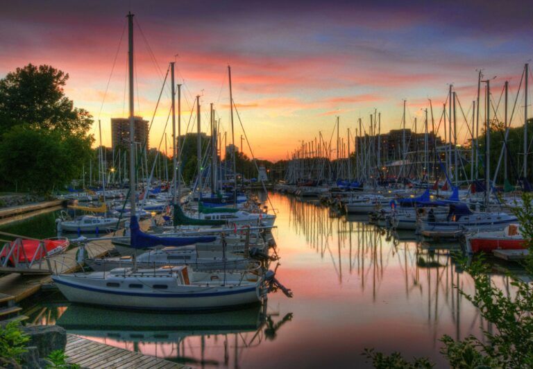 A bunch of sailboats are docked in a harbor at sunset.