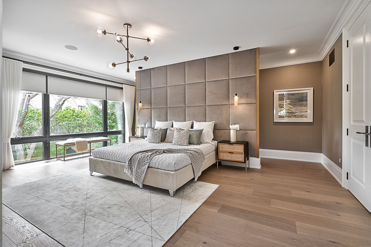 Large primary bedroom with neutral bedding, 2 side tables, a bench and a rug.