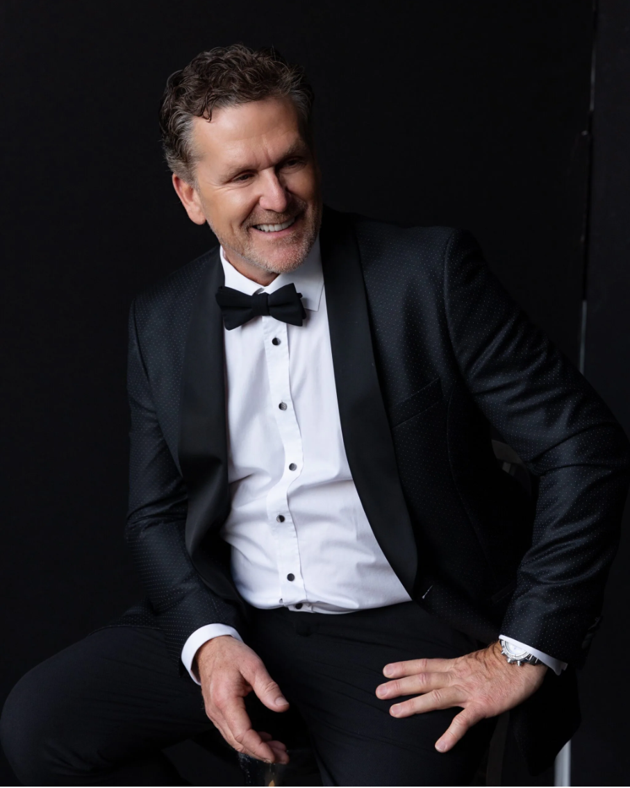 A man in a tuxedo and bow tie is sitting on a chair