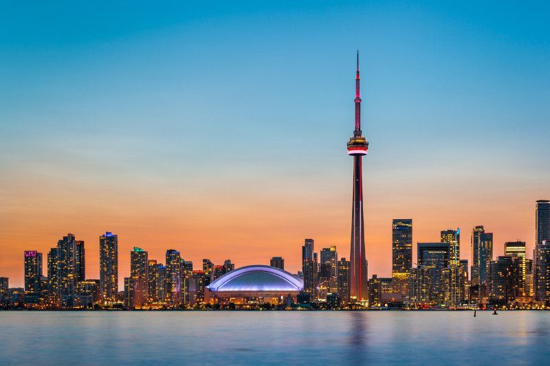 A city skyline with the cn tower in the foreground and a large body of water in the background.