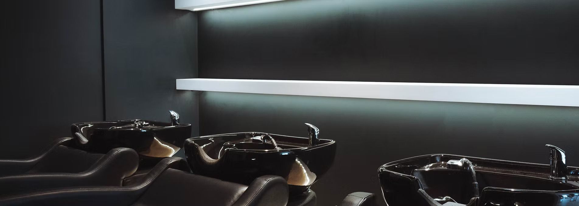 A row of black hair wash sinks in a hair salon.