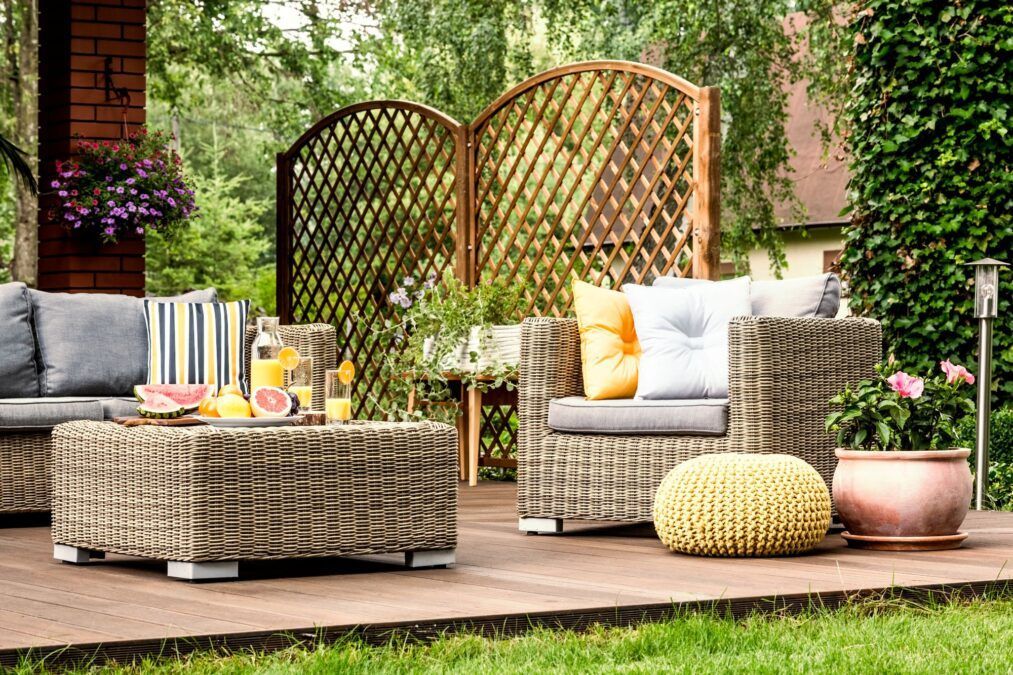 Exterior photo showcasing a beautiful backyard with wicker furniture, a privacy screen, vines and a deck.