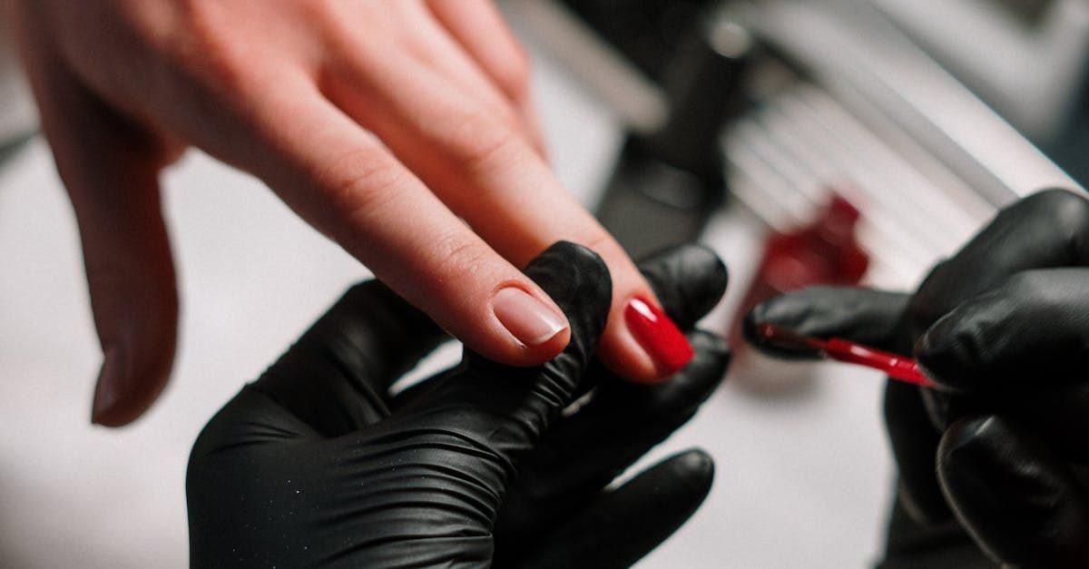 A woman is getting her nails painted by a man in black gloves.