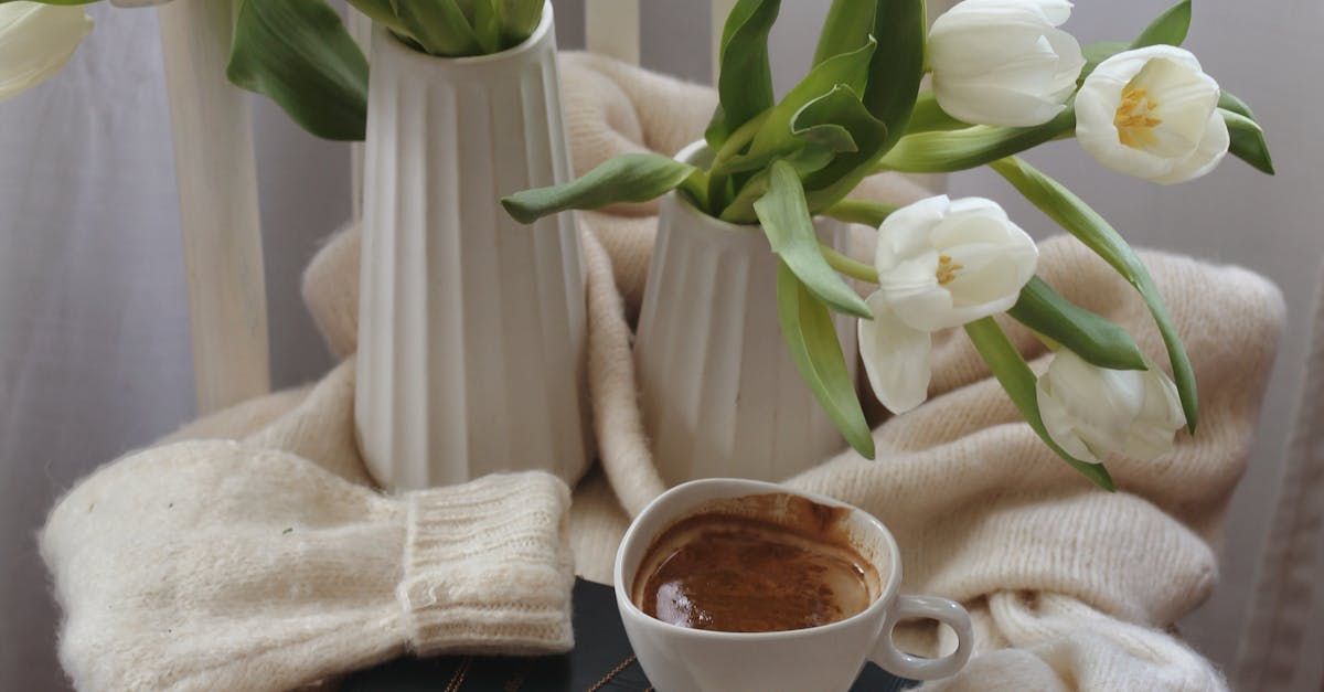 A cup of coffee is sitting on a table next to a vase of flowers.