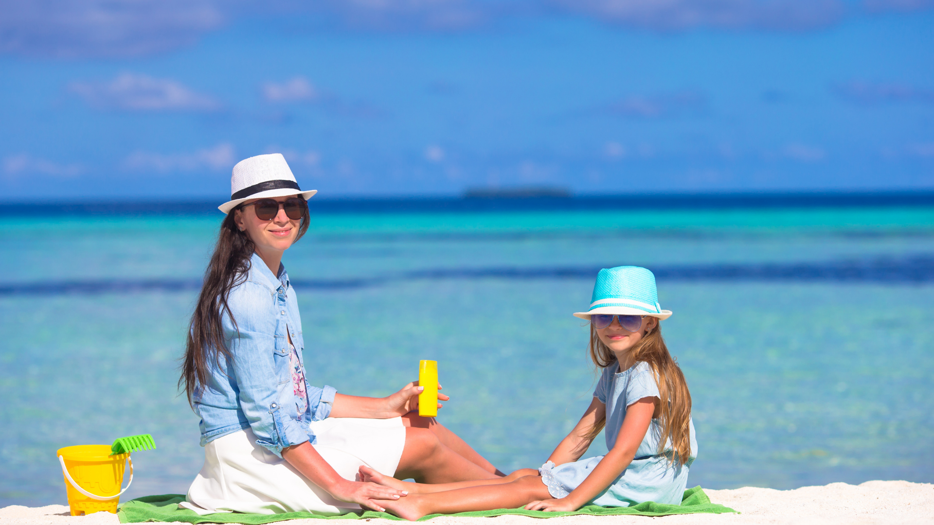 a woman and a little girl are sitting on a blanket on the beach .