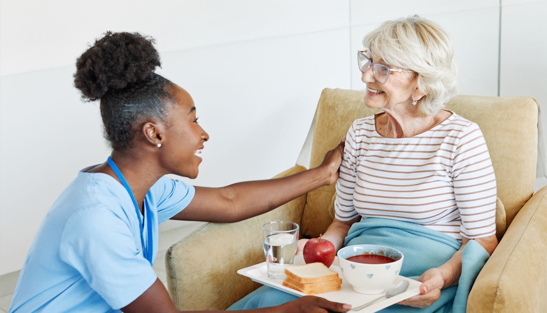Nurse comforts senior with meal tray, indoors.