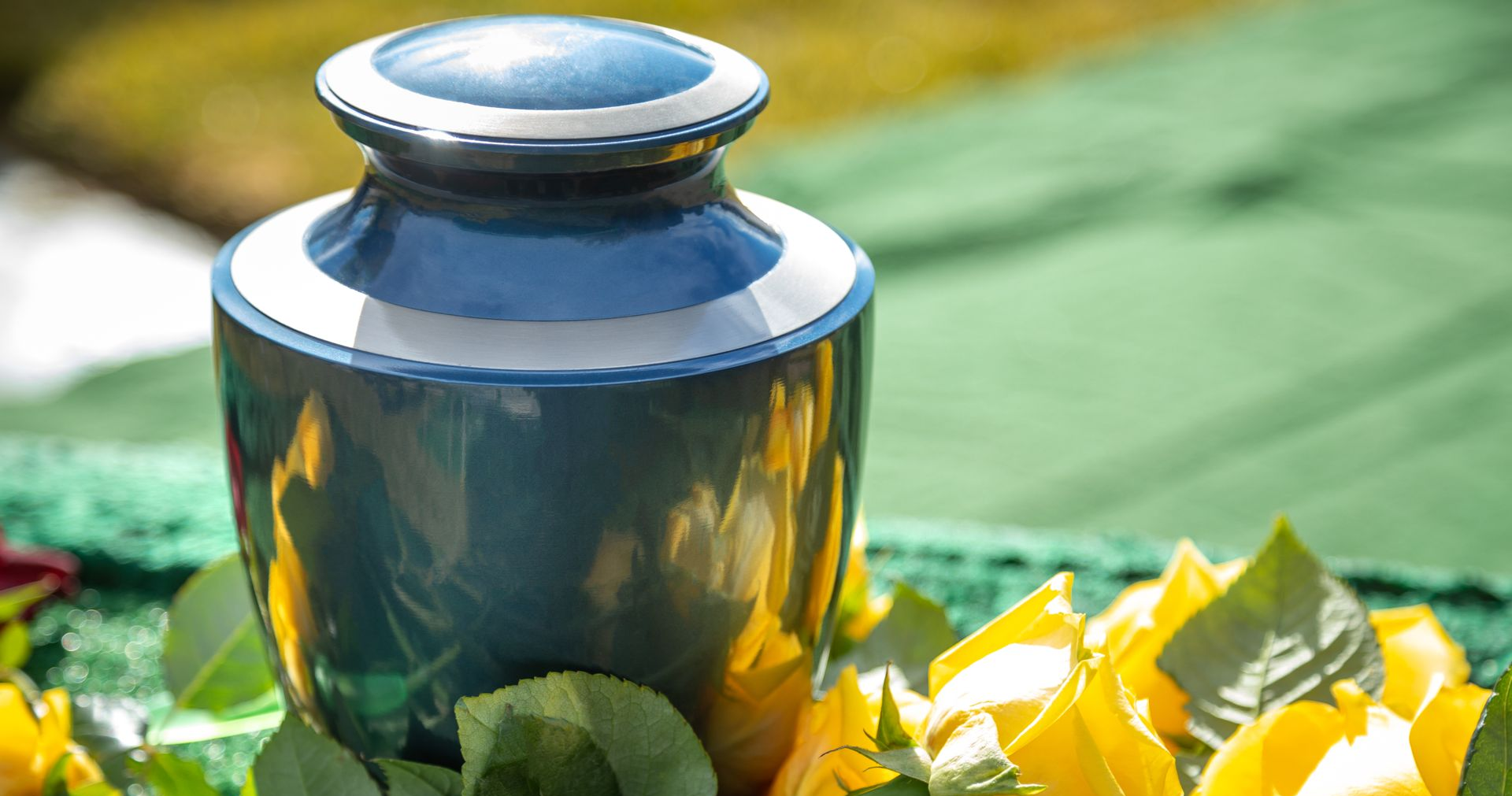 Blue ceramic vase with reflective finish among green leaves and yellow flowers outdoors