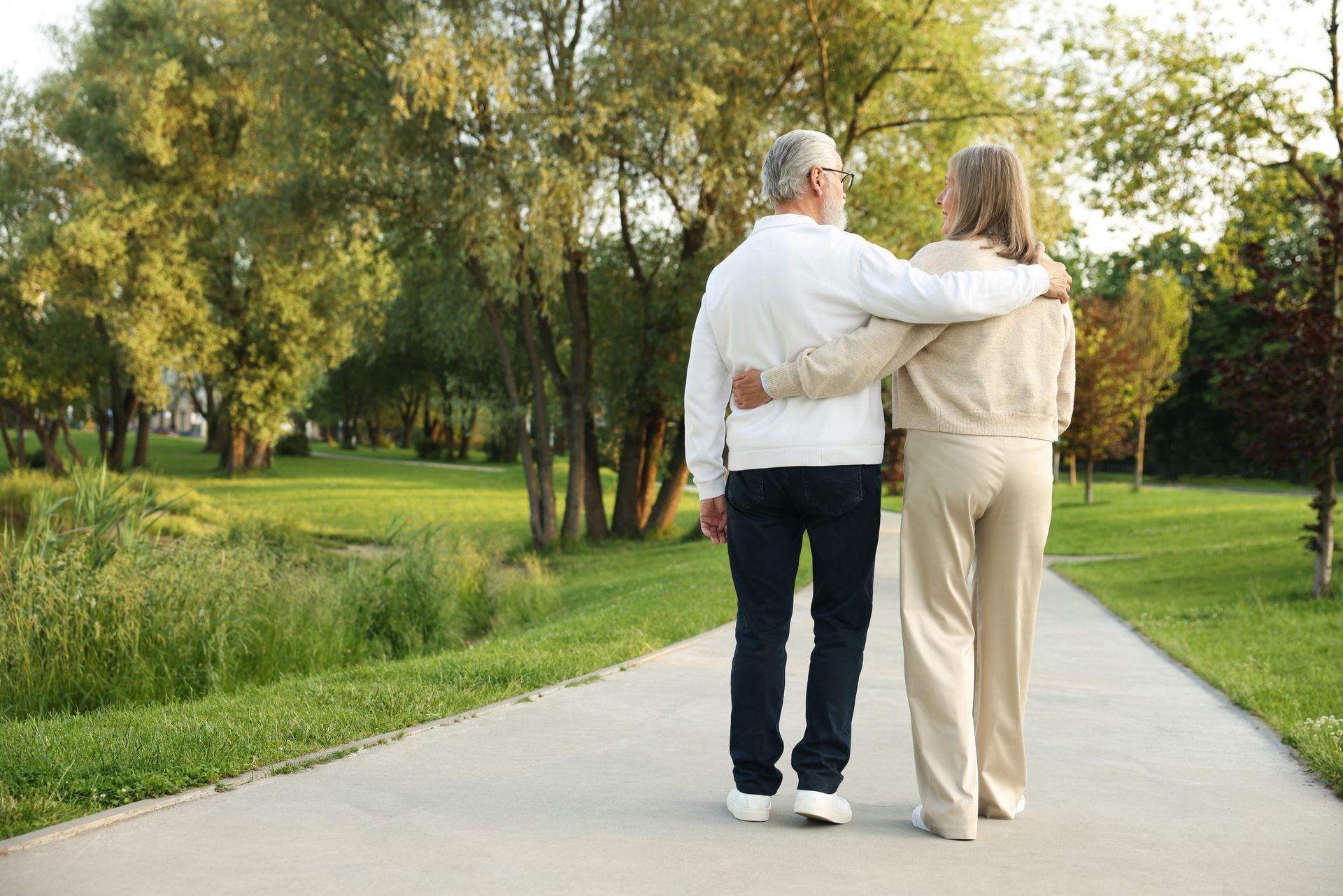 Two people walking arm in arm on a tree-lined park path in daylight
