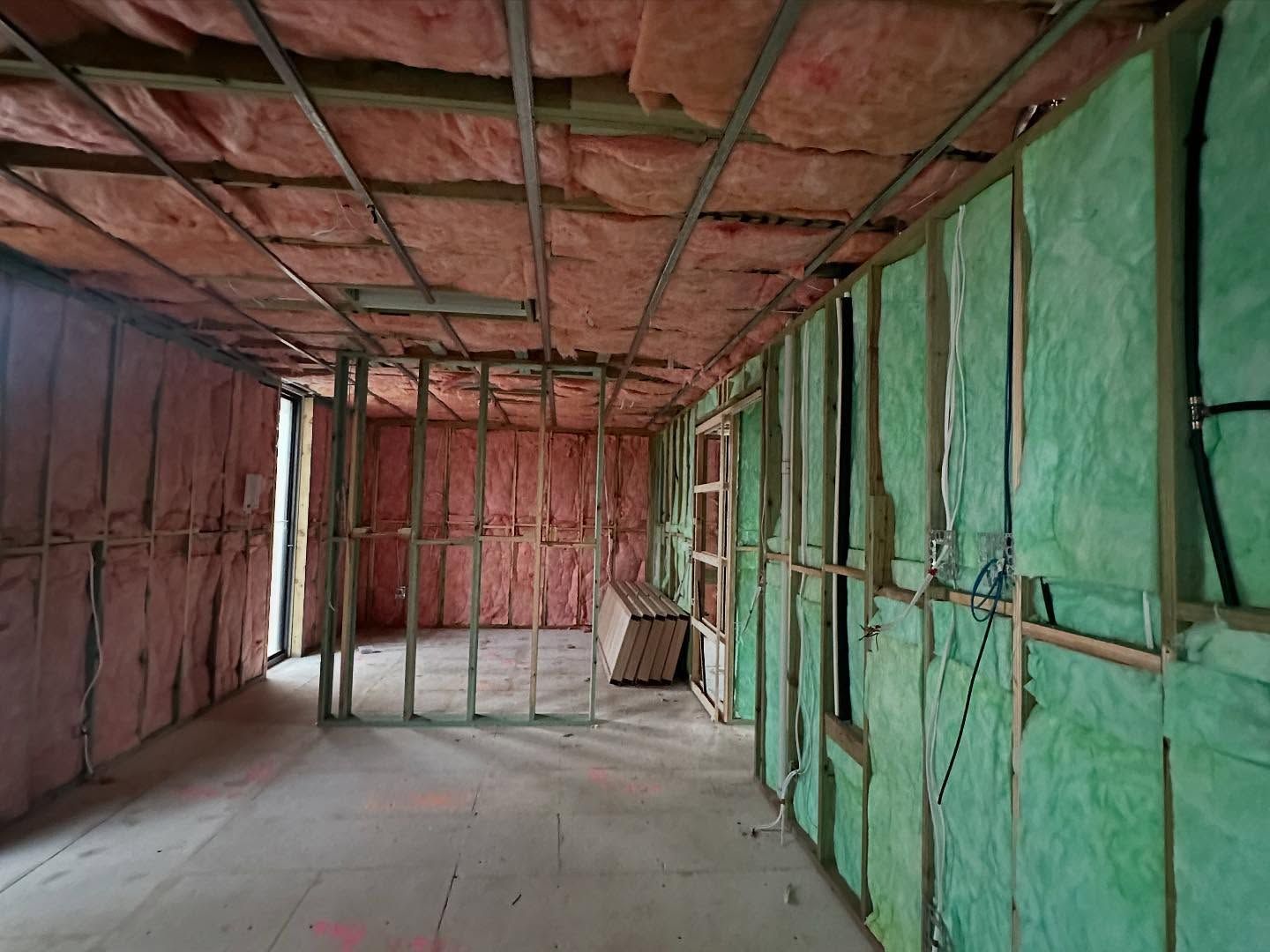 Interior of a room under construction with pink and green insulation between wooden framing.