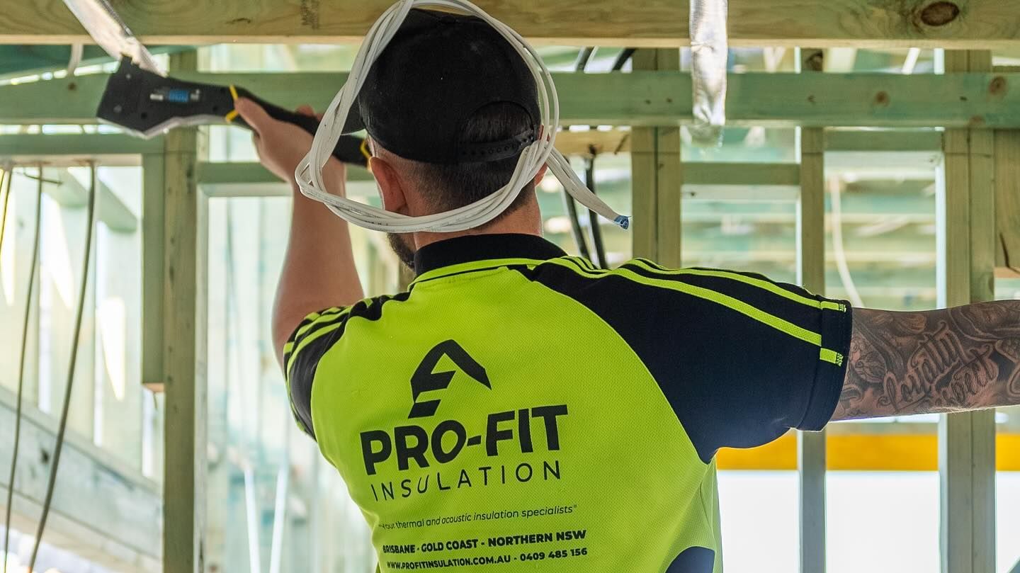 Construction worker installing insulation wearing a neon green and navy shirt with