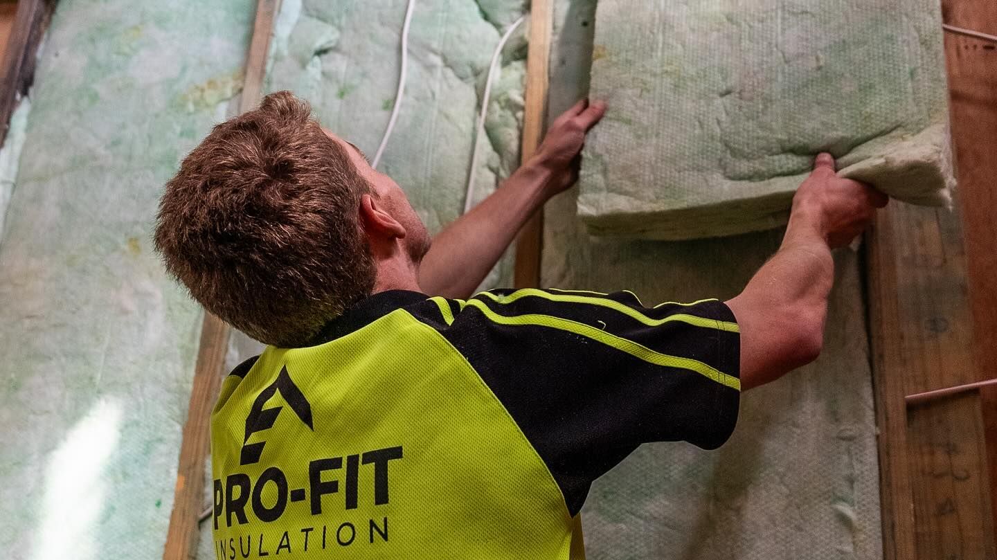 Man installing insulation between wooden wall studs.