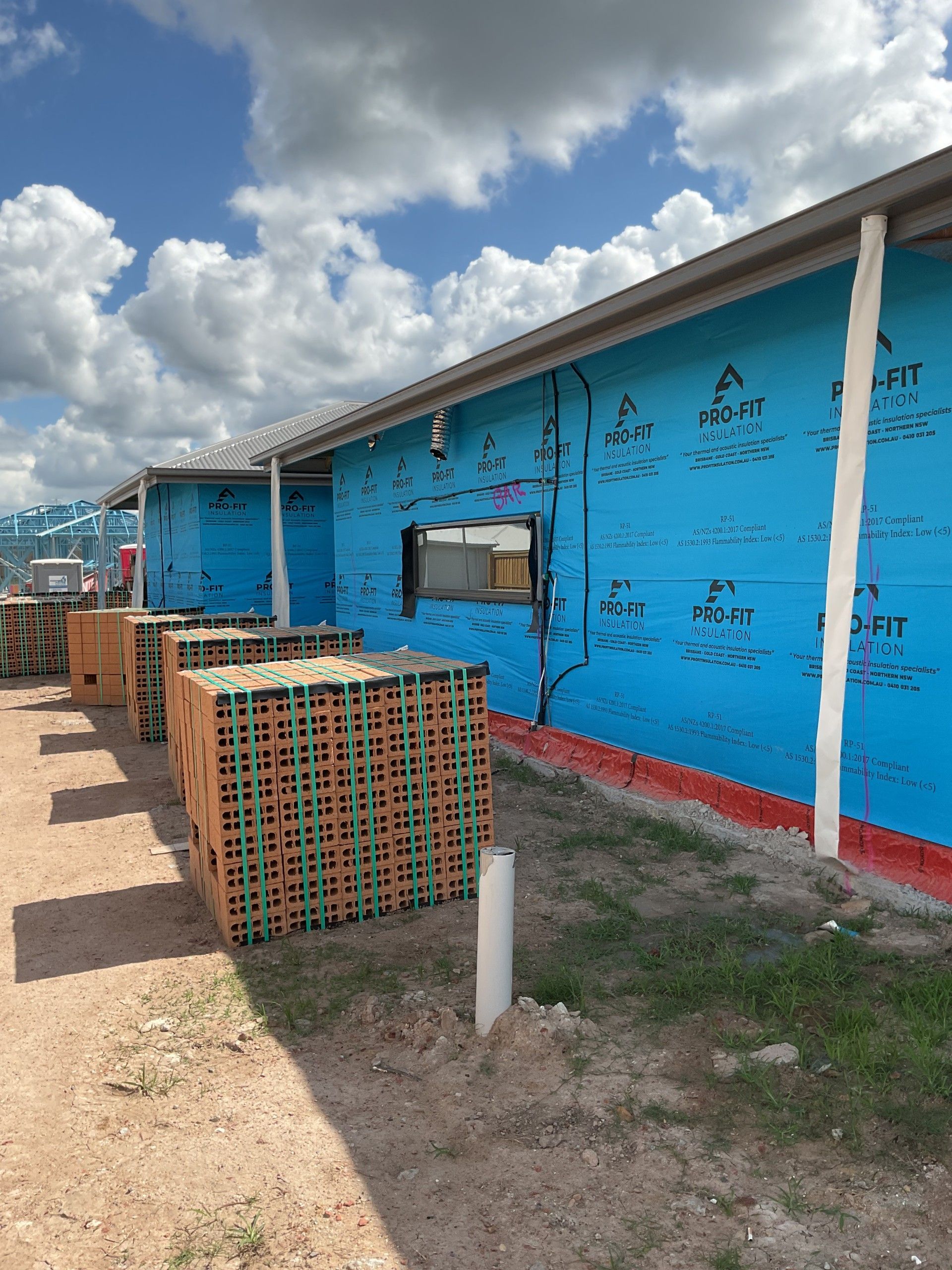 Construction site with blue building wrap, stacks of bricks, and a cloudy sky.