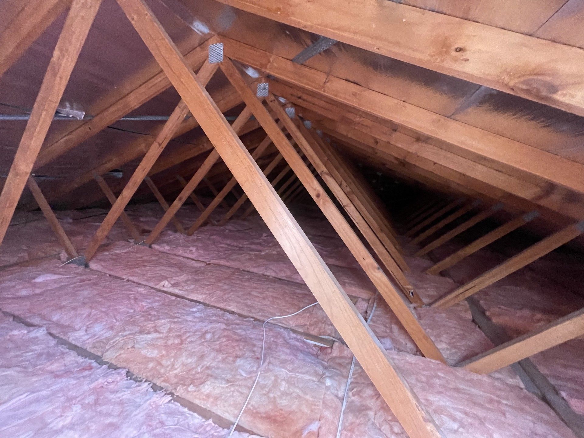 Wooden attic trusses with pink insulation.