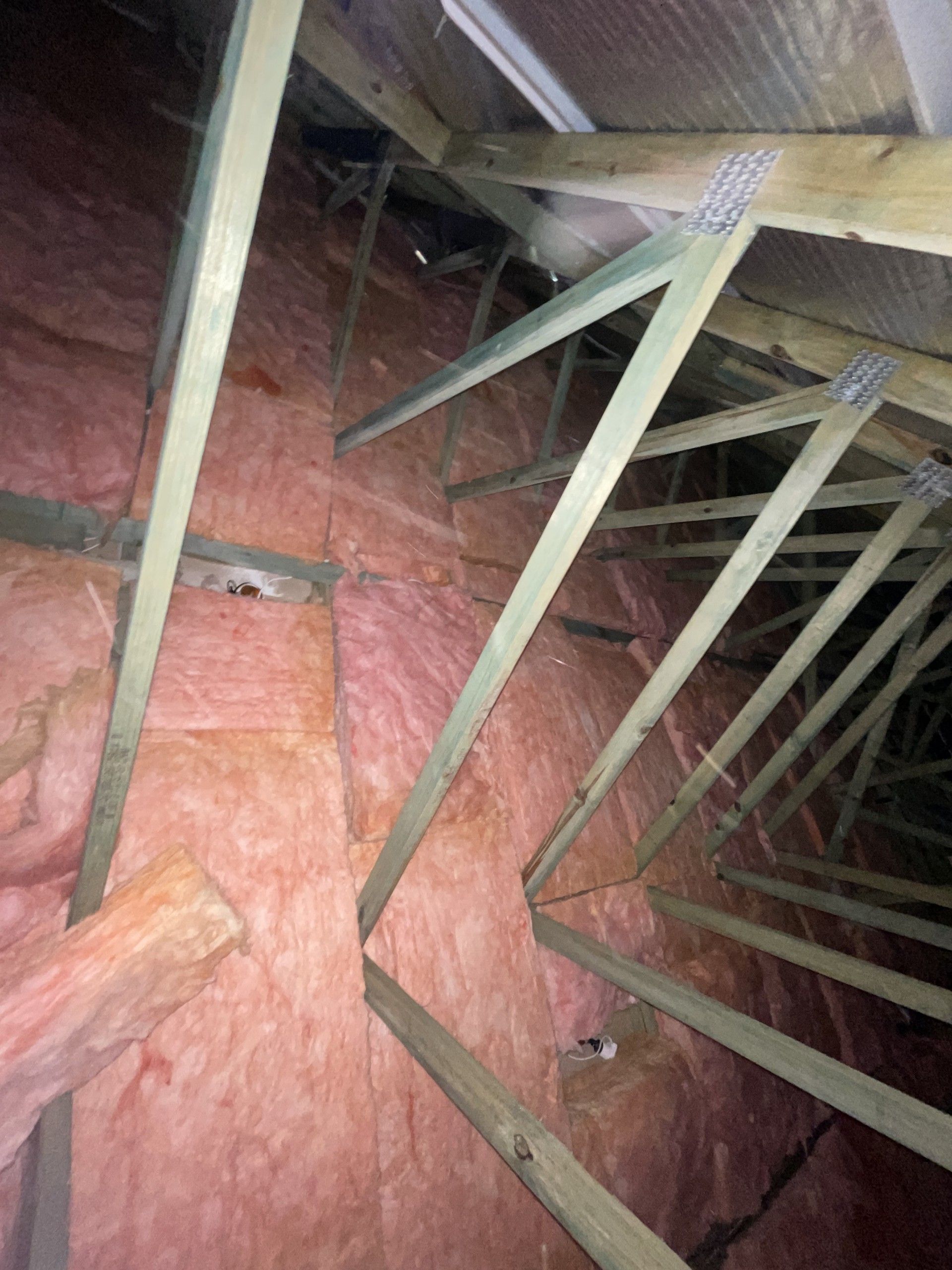 Pink insulation fills an attic space, wooden rafters support the roof.