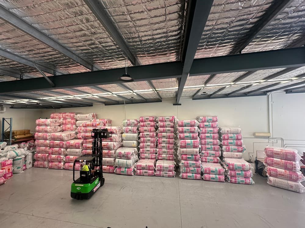 Warehouse with pink insulation rolls stacked high. A forklift is parked nearby.