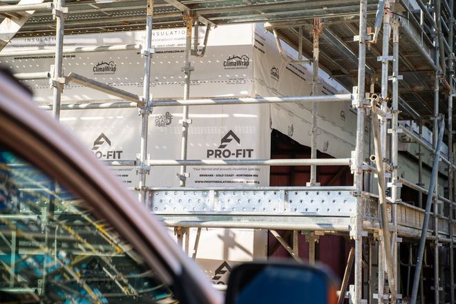 Scaffolding surrounds a building under construction, with "PRO-FIT" branded insulation visible.