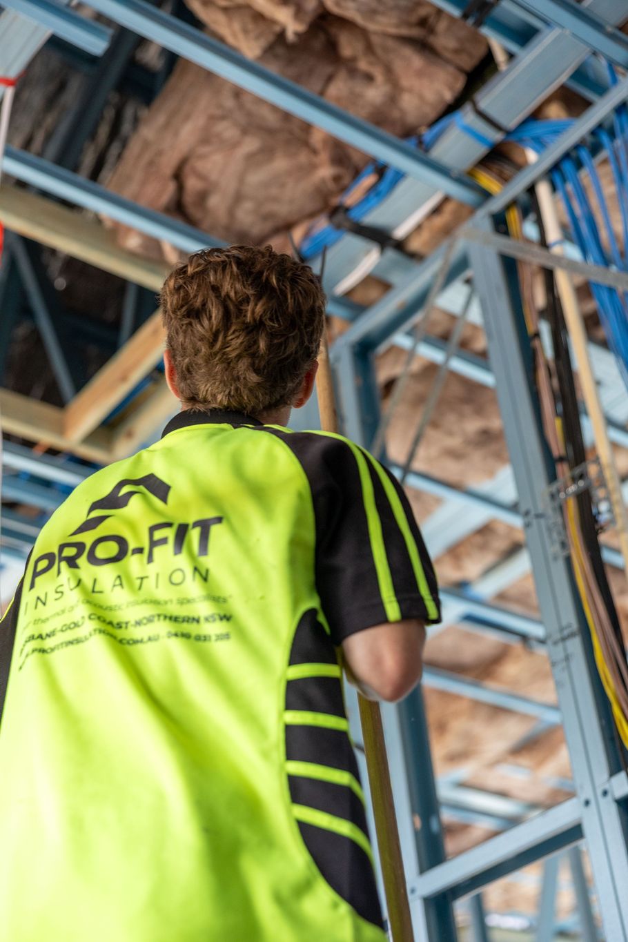 Worker in a neon yellow safety vest looking up at scaffolding and insulation on a construction site