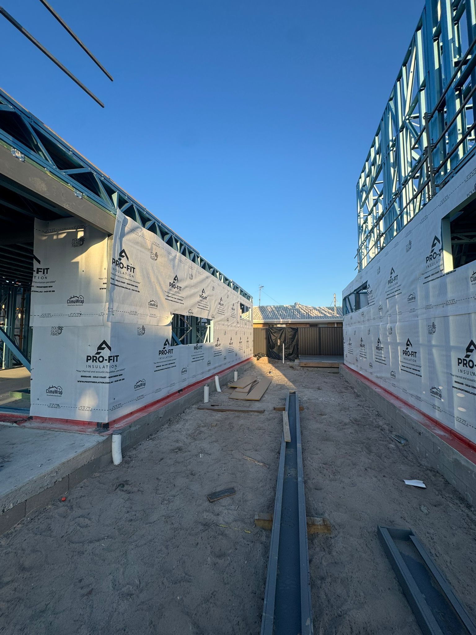 Construction site: two building frames with blue sky. Walls are covered in white sheathing.