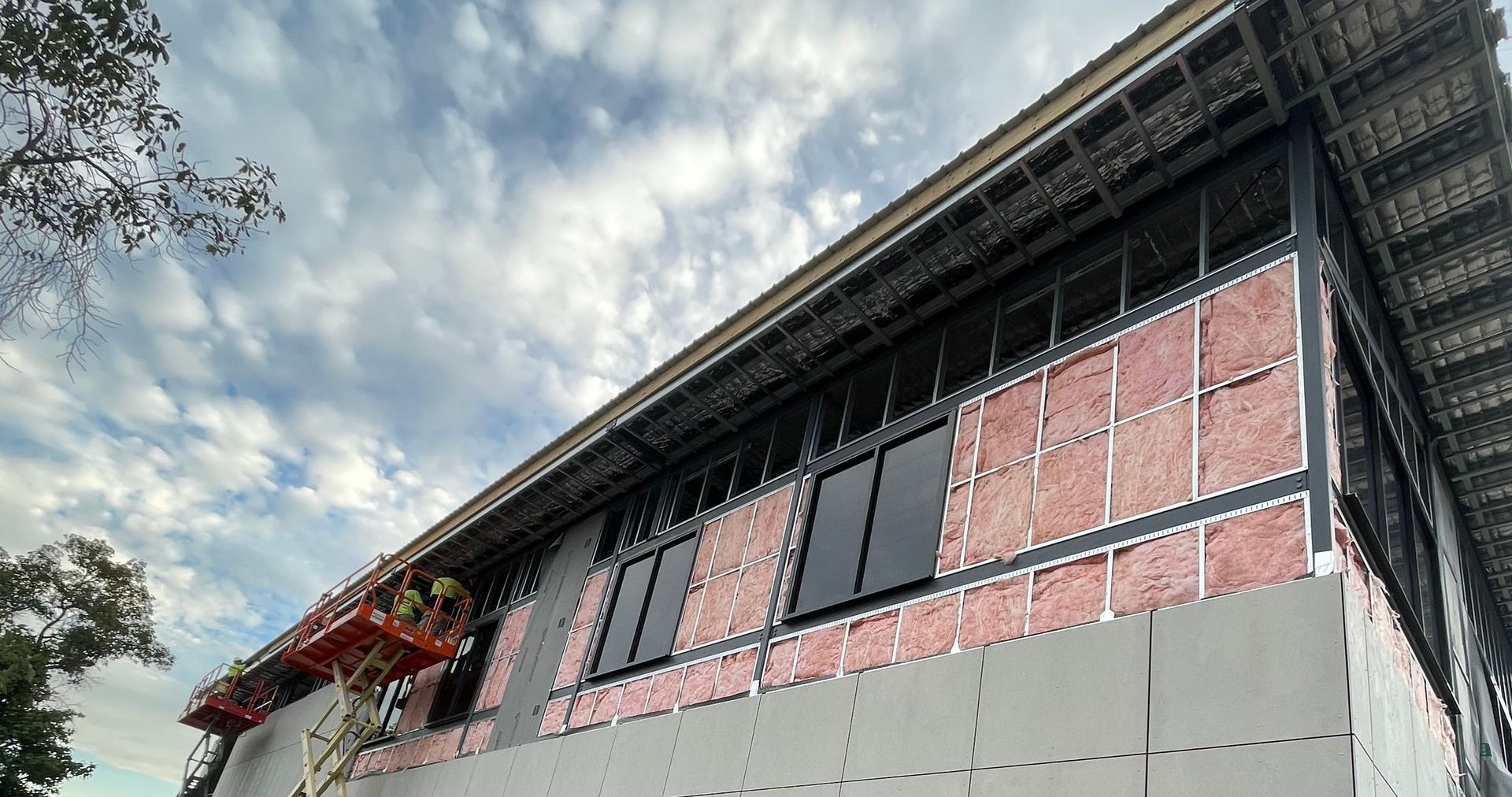 Building exterior under construction with exposed insulation and windows. Cloudy sky.