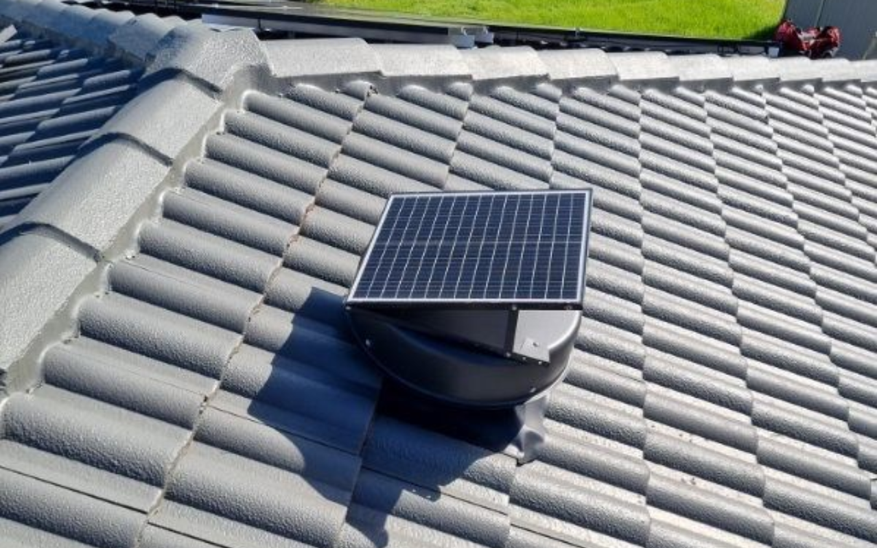Solar-powered roof vent installed on a gray tiled roof. The vent has a small solar panel on top.