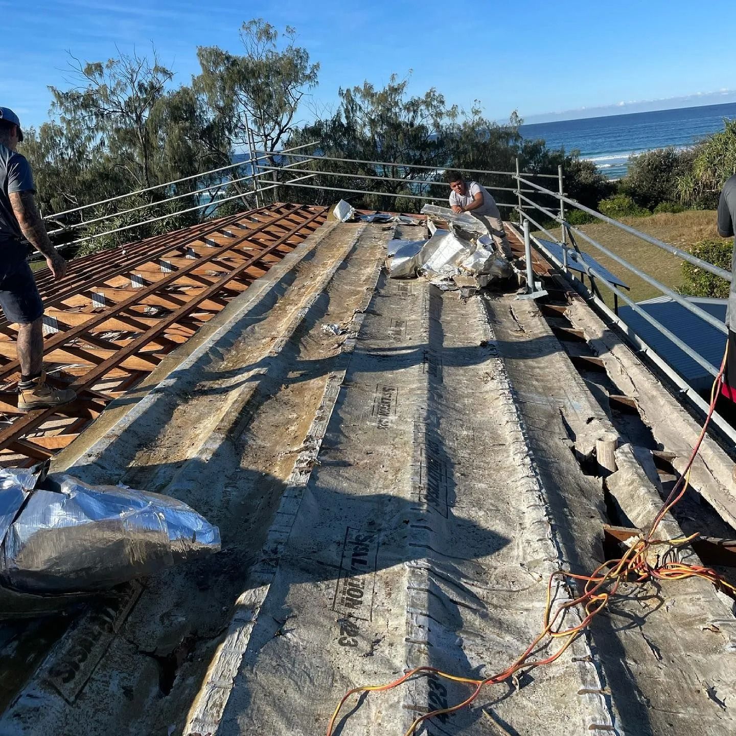 Workers removing old roofing on a structure with ocean view.