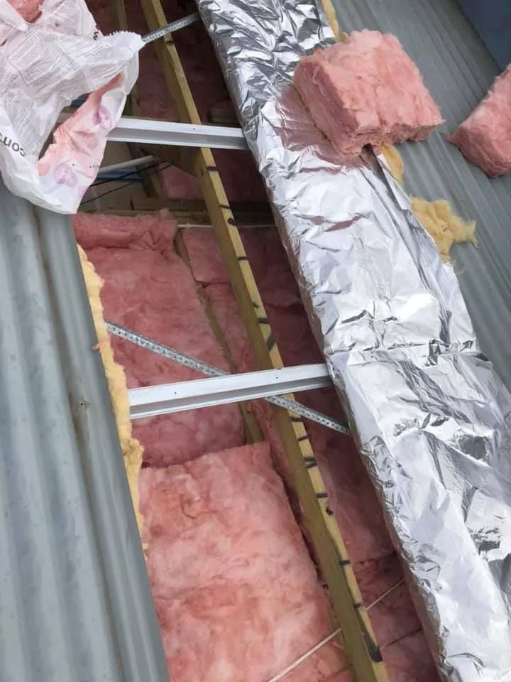 Pink insulation batts installed in a roof cavity, with foil and metal supports visible.