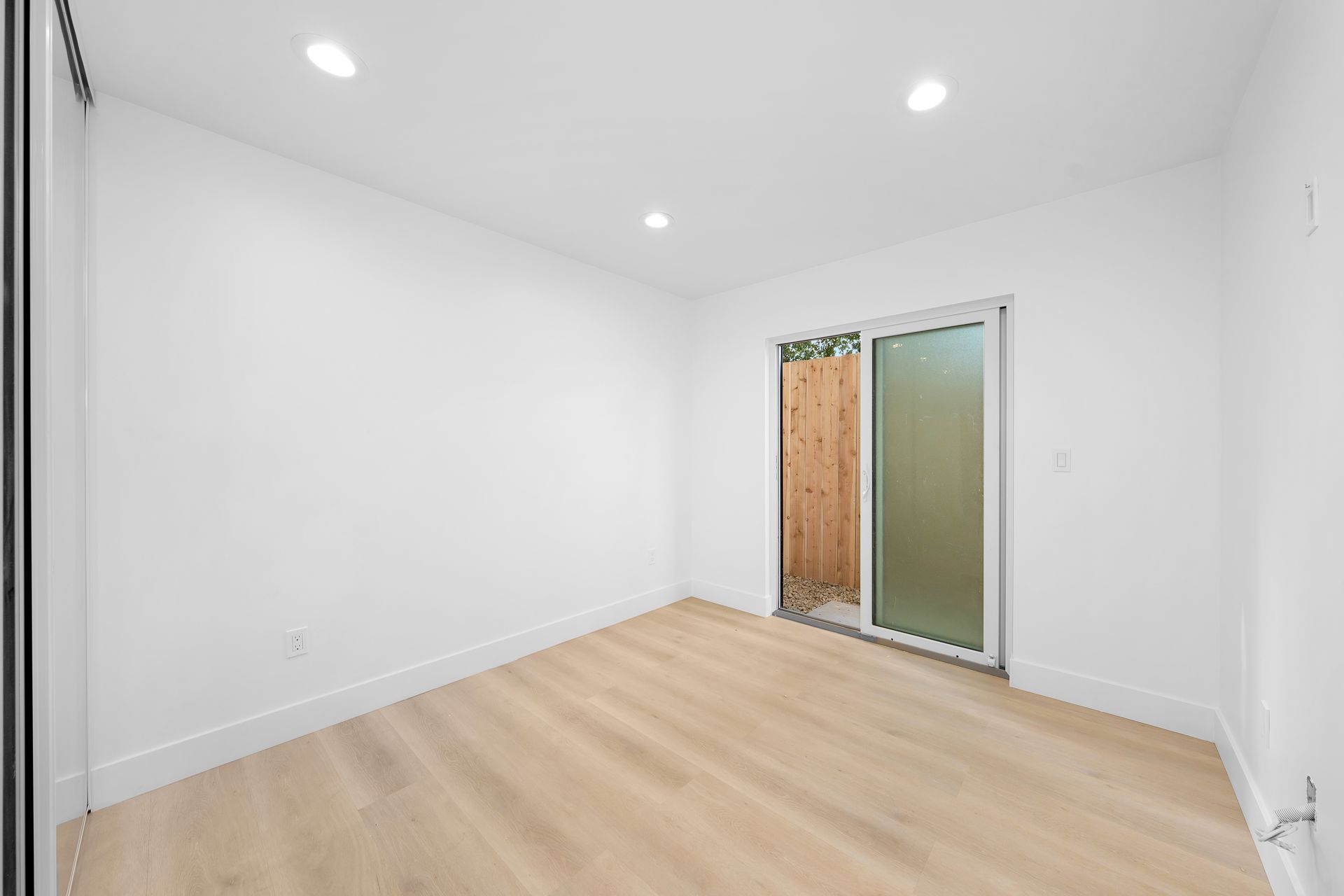 An empty room with hardwood floors and a sliding glass door.