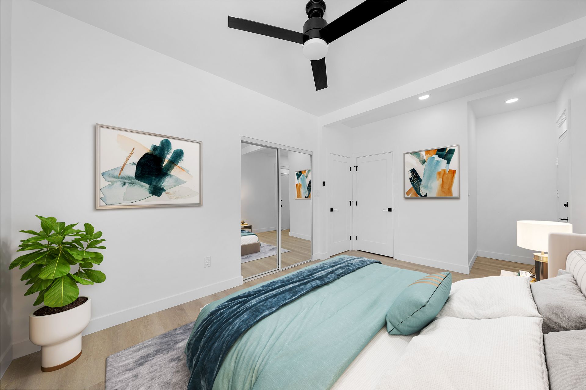 A bedroom with a bed , ceiling fan , mirror and paintings on the wall.