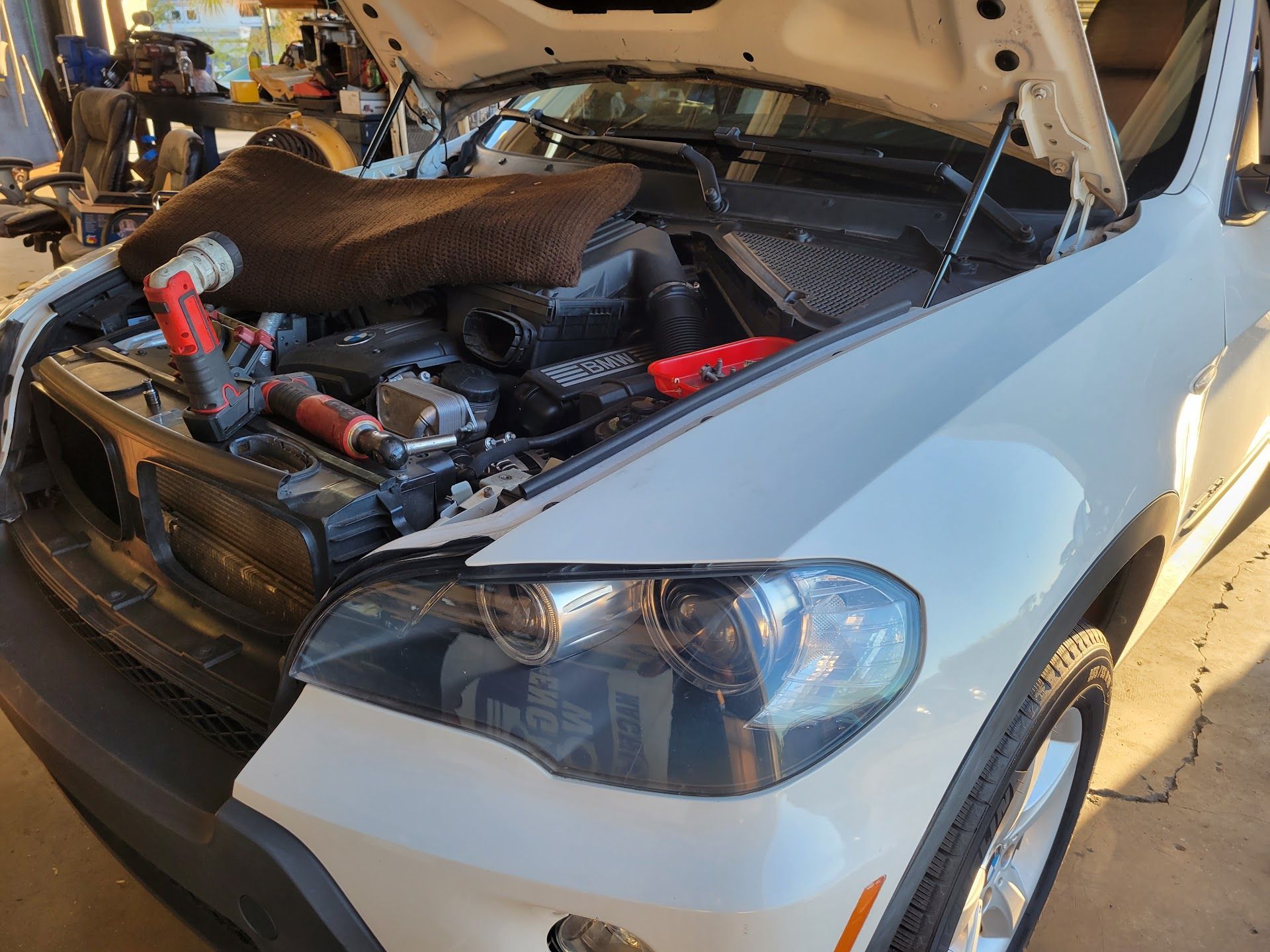 White BMW SUV with hood open, tools visible, engine bay exposed | St. Lucie Auto Dynamics