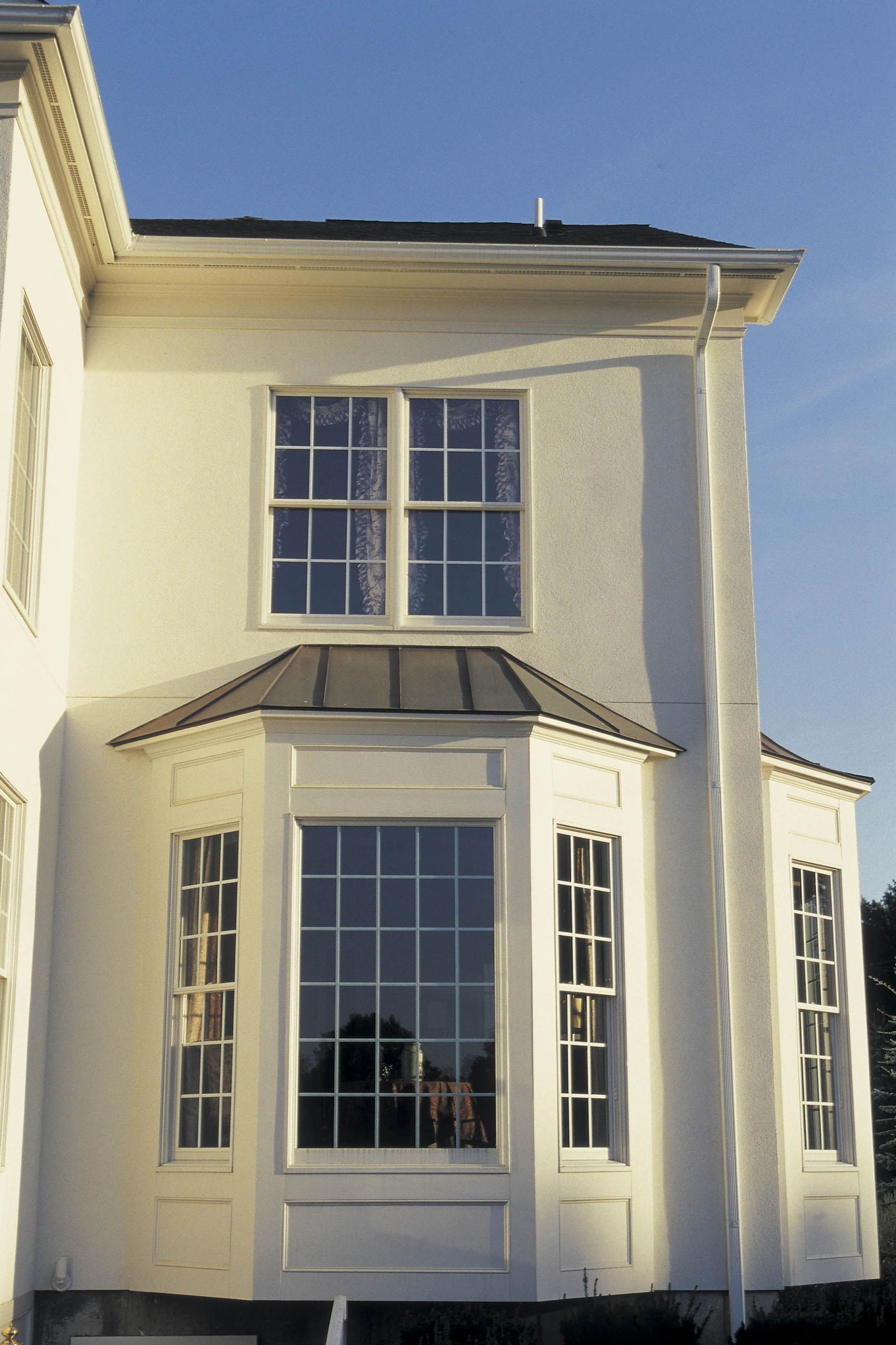 White house facade with tall bay windows and dark roof trim under a clear blue sky