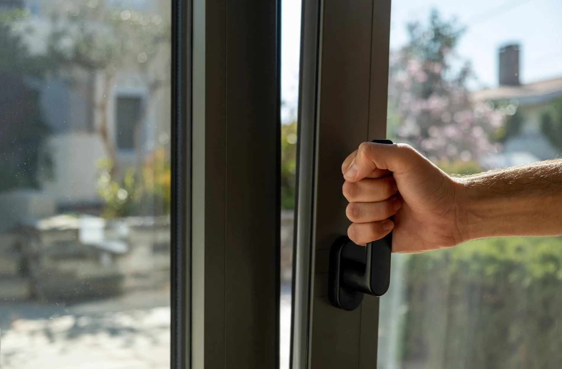 Hand gripping a black sliding glass door handle with a bright outdoor view beyond