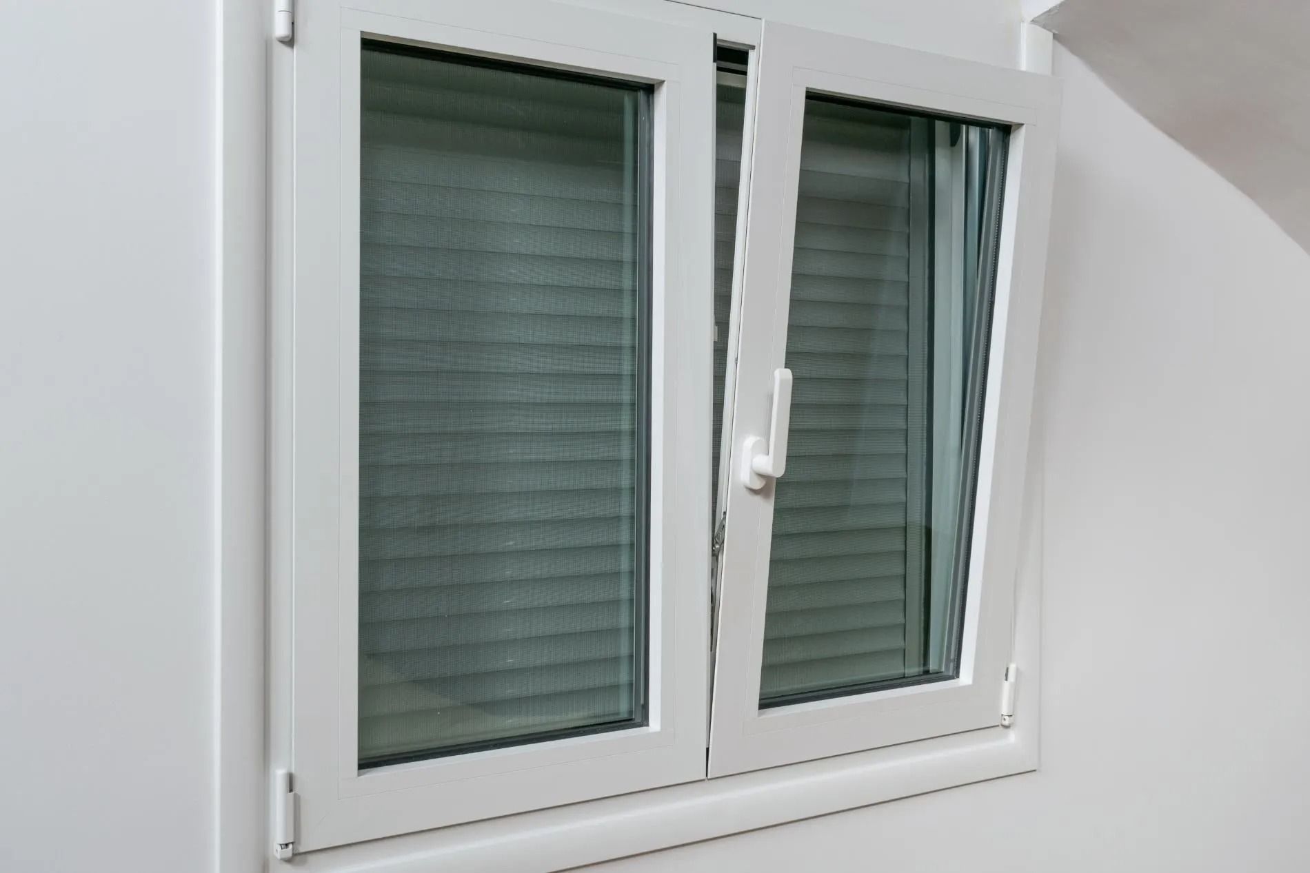 White-framed window with closed green blinds on a slanted wall