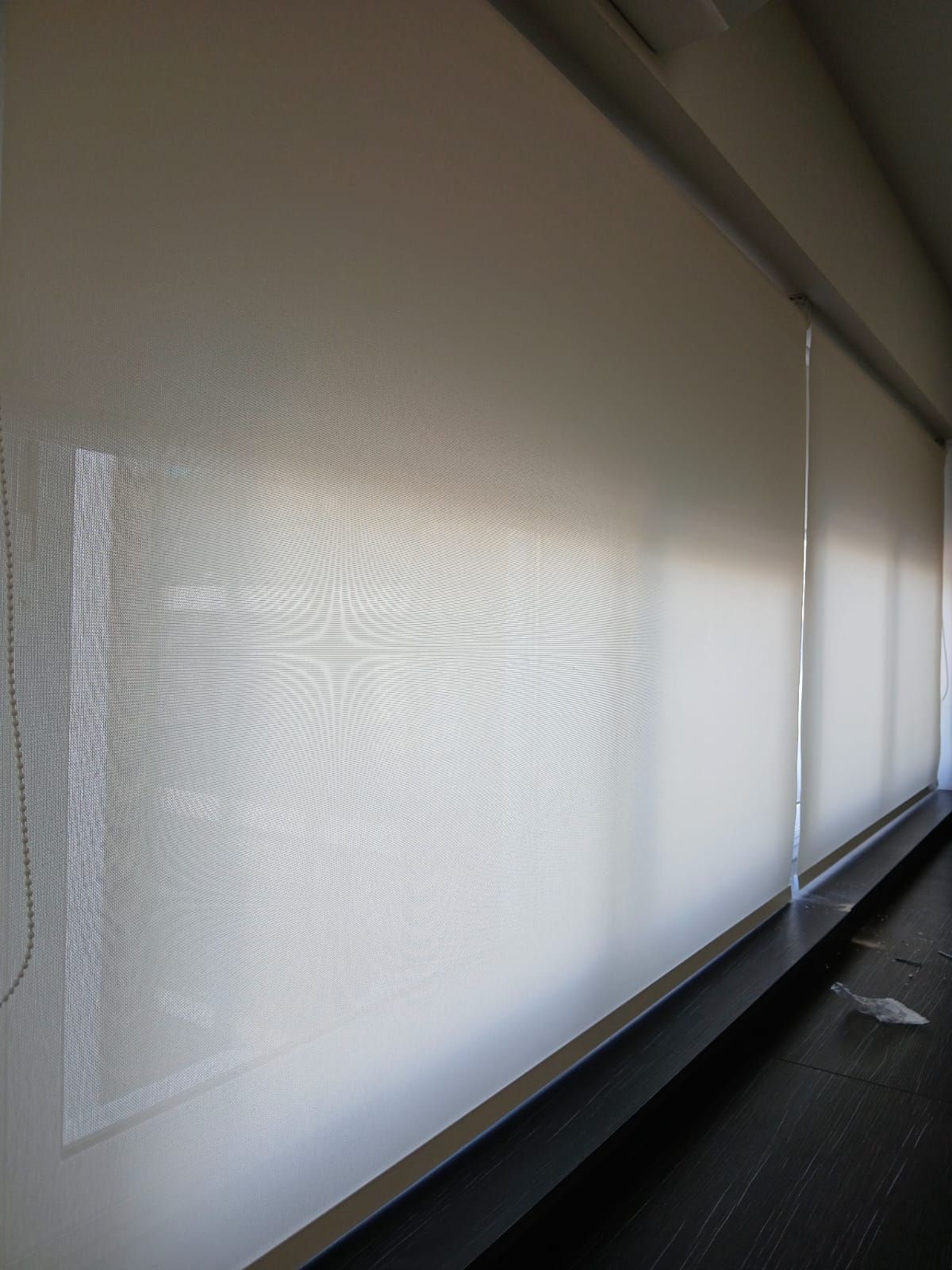 Persianas blancas que cubren una ventana en un pasillo oscuro, con luz solar filtrándose a través de ella.
