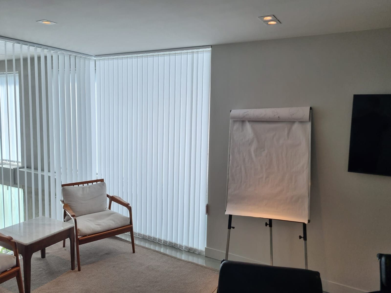 Sala de estar moderna con puertas corredizas de vidrio, una silla, una mesa, un rotafolio y un televisor montado en la pared.