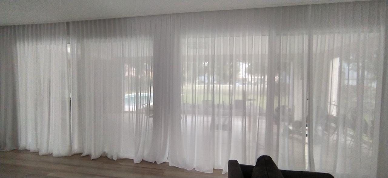 Cortinas blancas translúcidas que cubren grandes ventanales en una habitación luminosa.